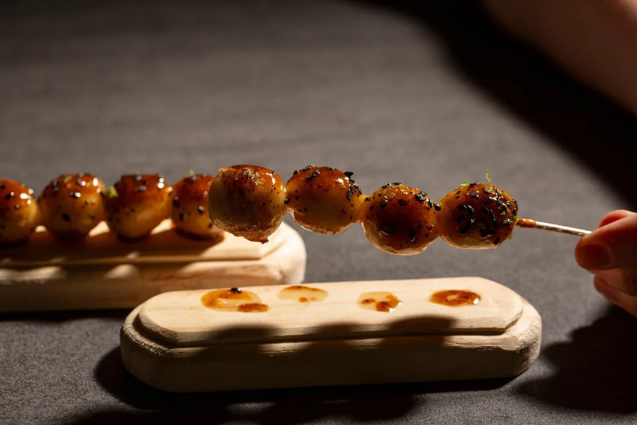 A skewer of glazed golden pieces resting over a pale wooden serving board