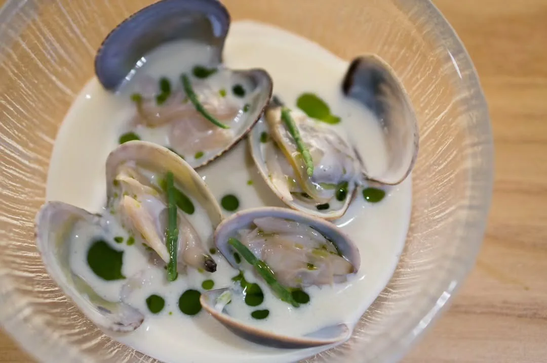 Clams in a pale broth in a glass bowl