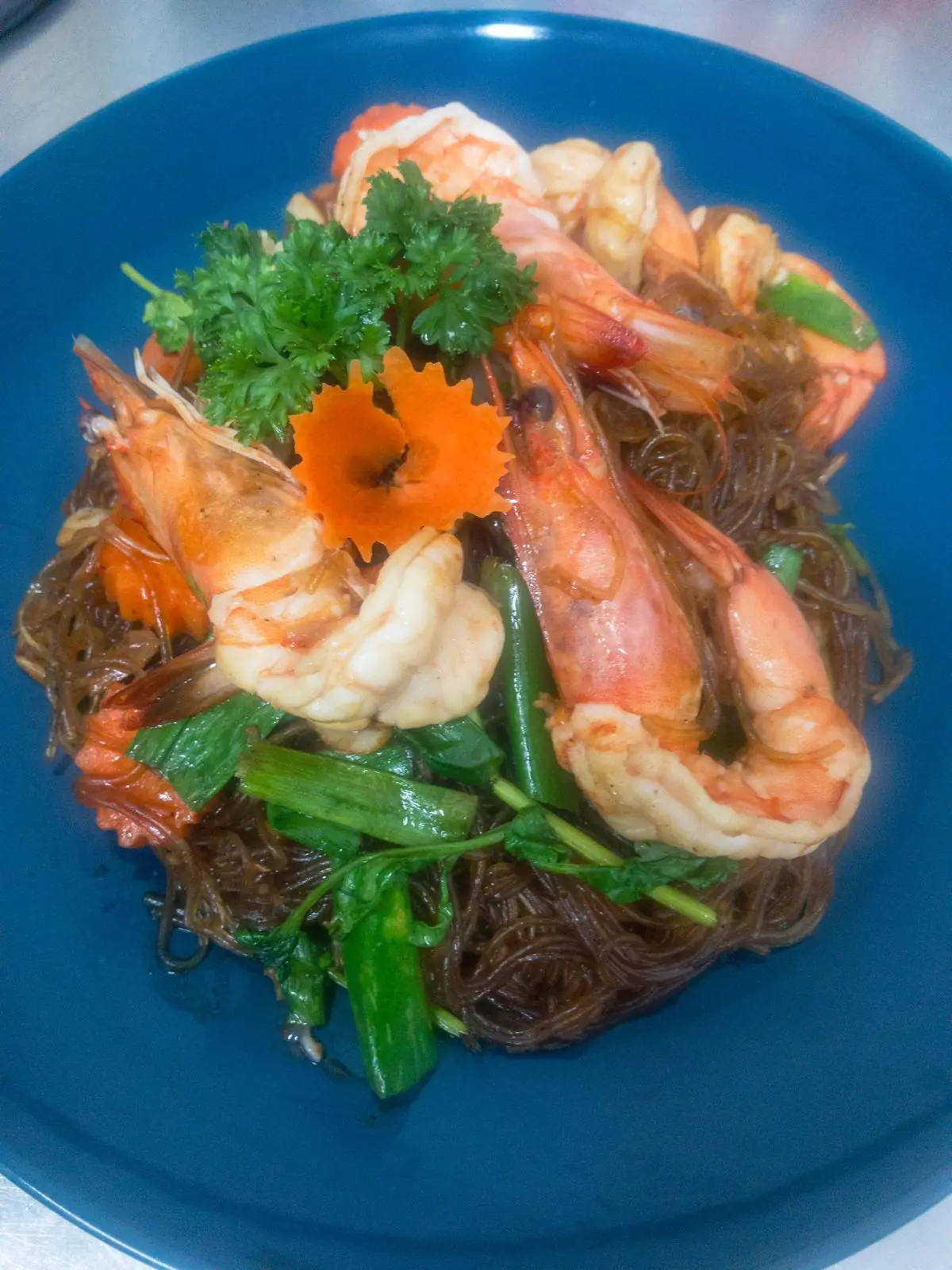 Stir-fried glass noodles with jumbo shrimp, green beans, and herbs on a blue plate at Restaurant Thai Rico