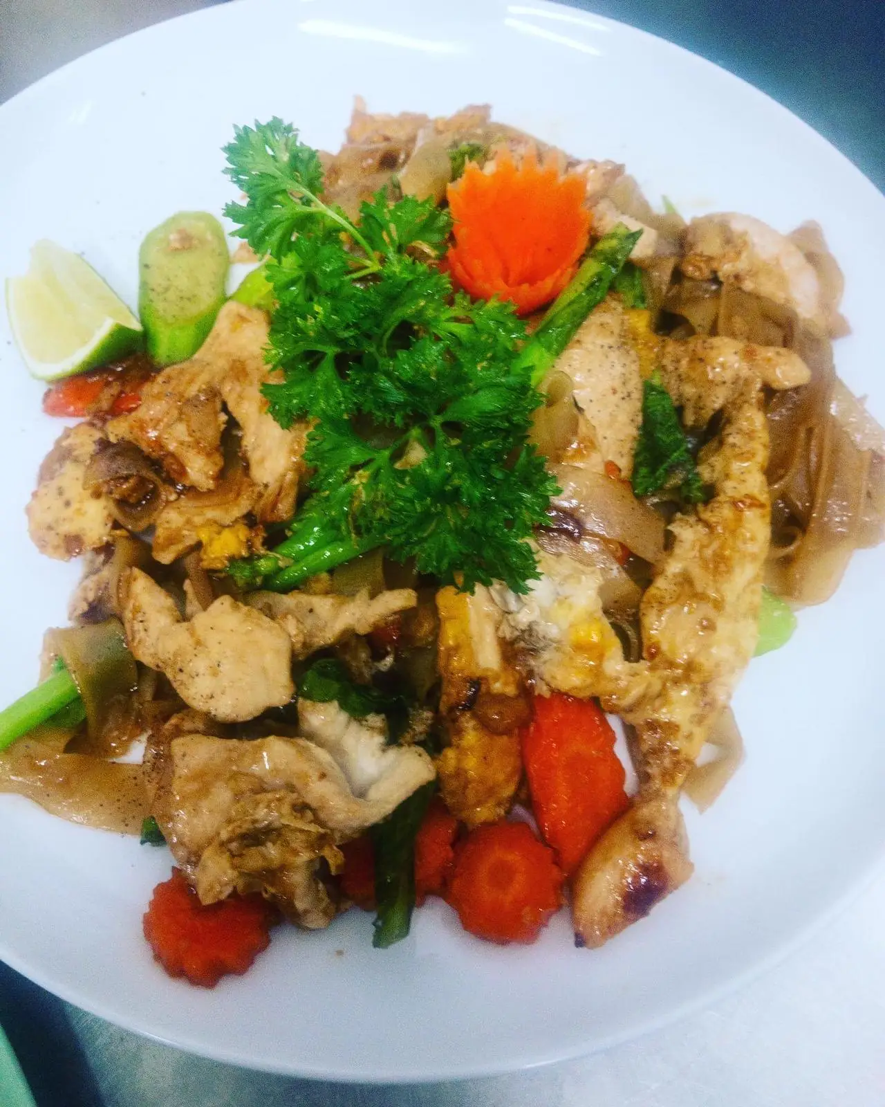 Pad see ew noodles with chicken, egg, and carrot garnish on a white plate at Restaurant Thai Rico