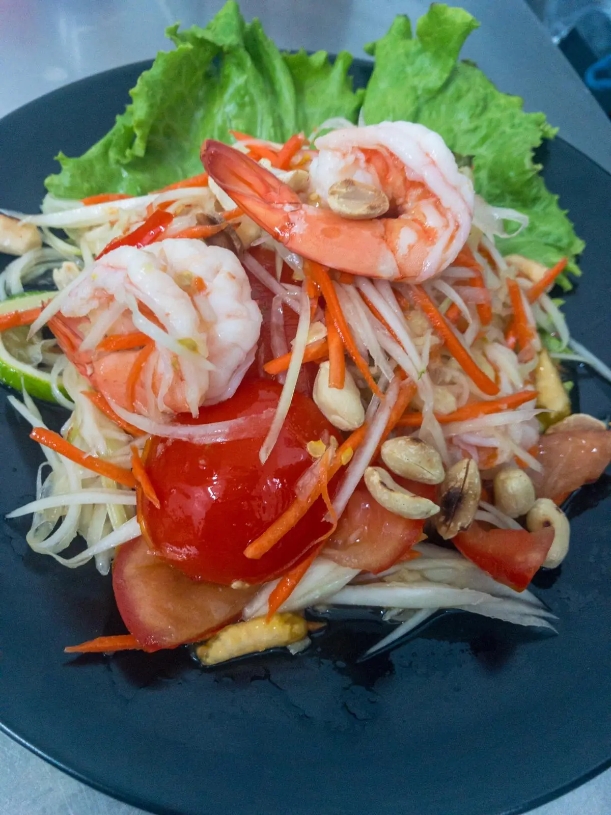 Papaya salad with shrimp, tomato, peanuts, and lettuce on a black plate at Restaurant Thai Rico