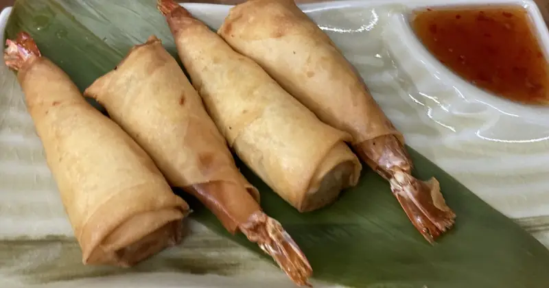 Crispy fried spring rolls wrapped around whole prawn tails on a banana leaf with sweet chili dipping sauce, Thai Zaap