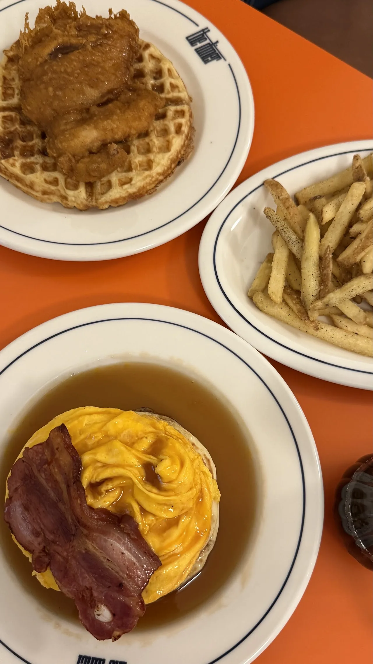 Three plates including waffles, fries, and a bacon-topped pastry
