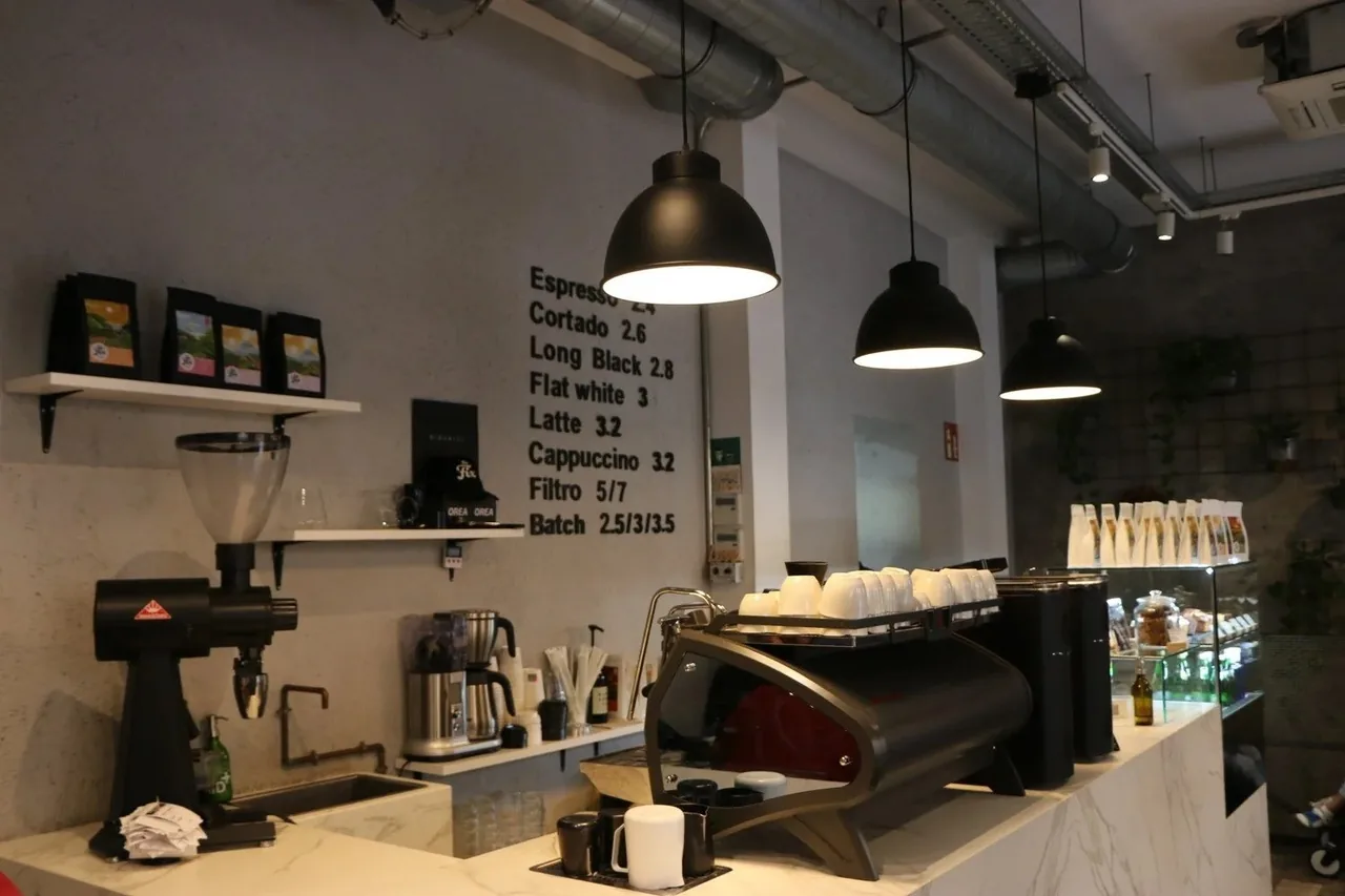 A cafe bar with an espresso machine, grinders and menu board on the wall above the counter