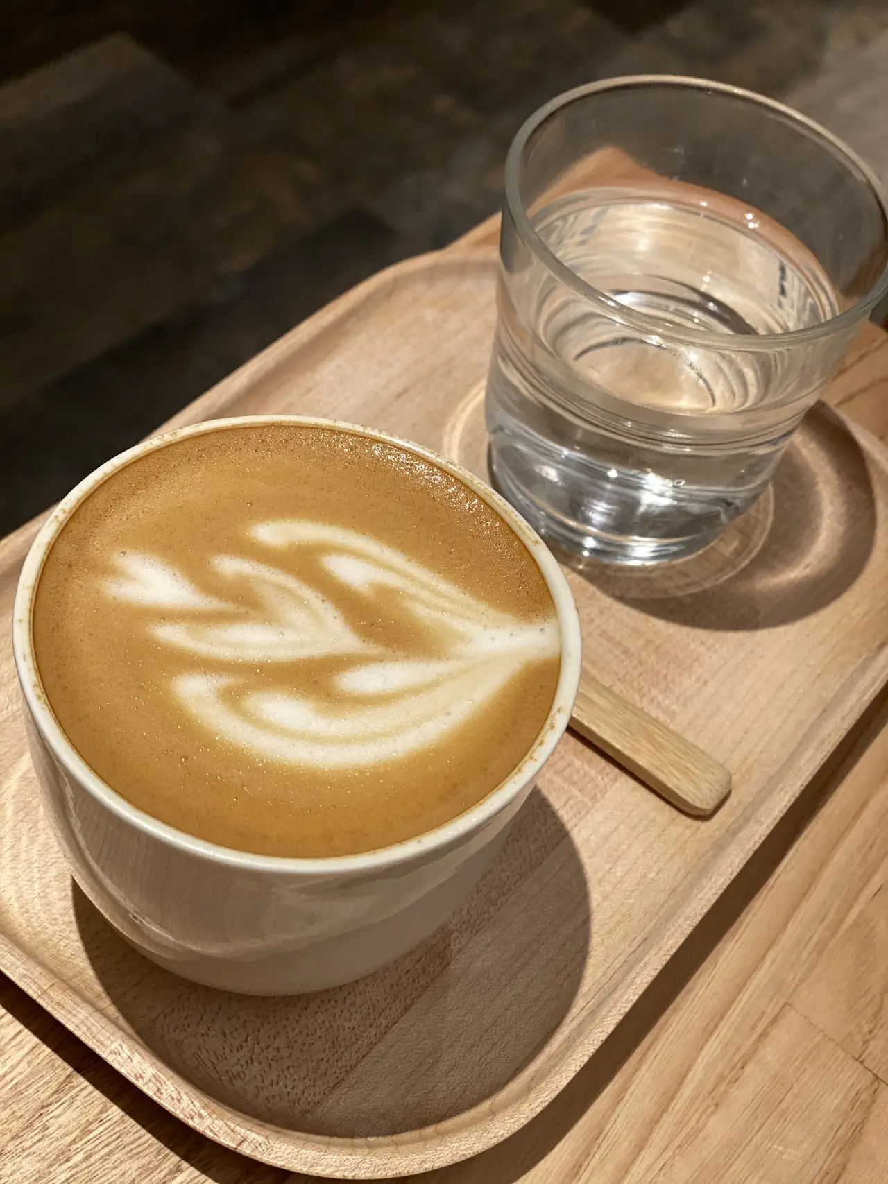 A latte with leaf-pattern art next to a small glass of water on a wooden tray.