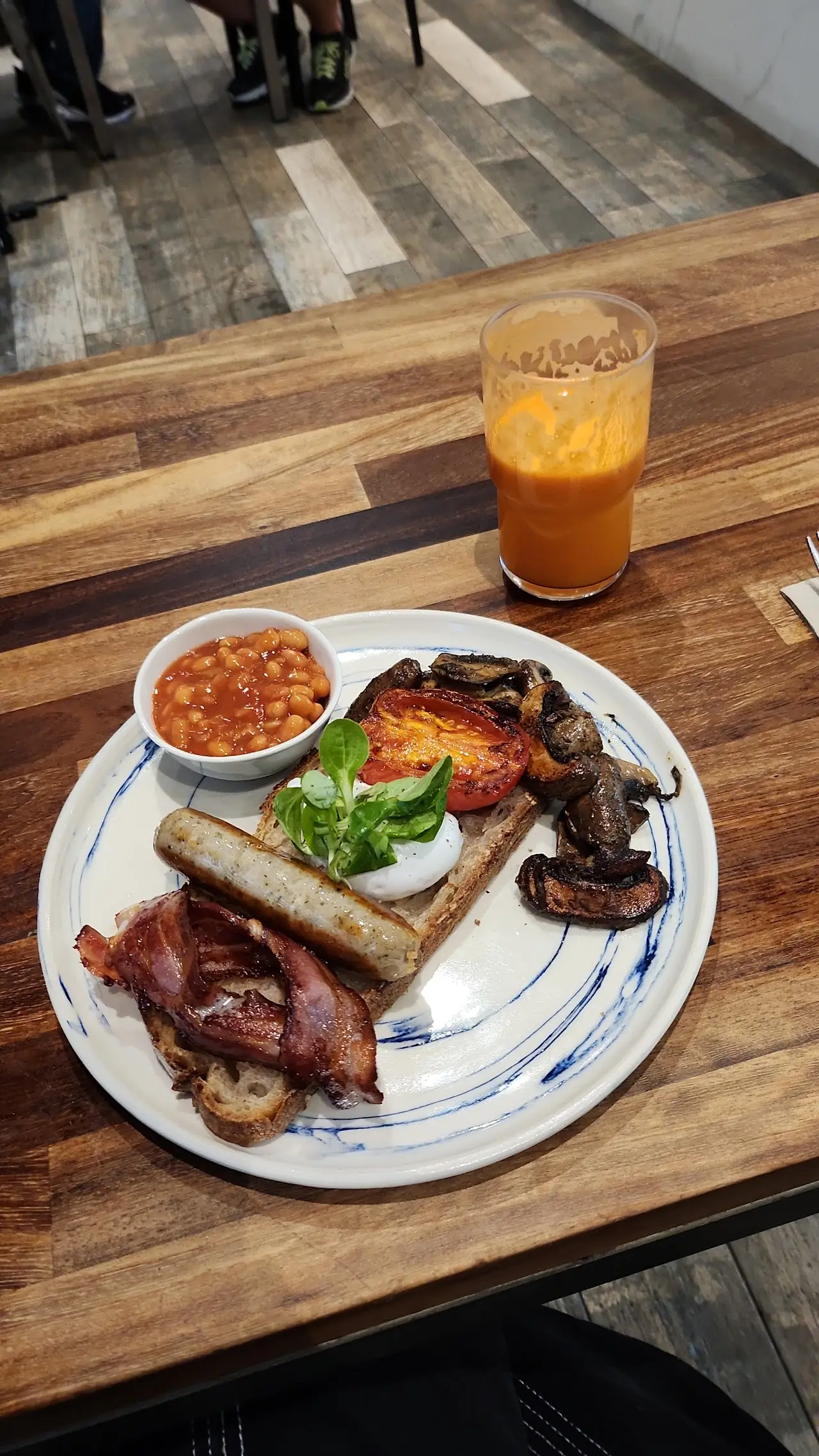 A breakfast plate with eggs, beans, bacon, and toast alongside a glass of orange juice.