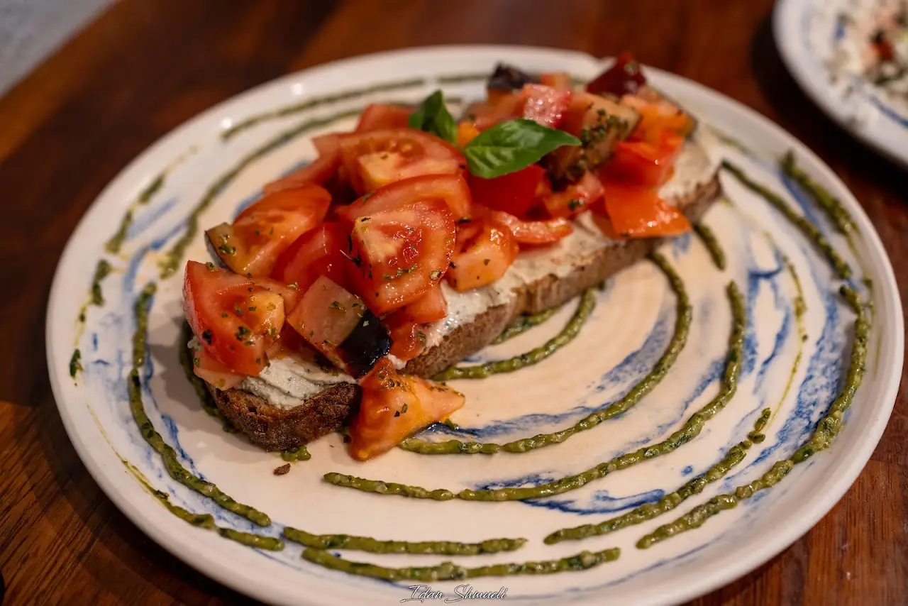 An open-faced tomato and basil toast drizzled with green sauce on a patterned plate.