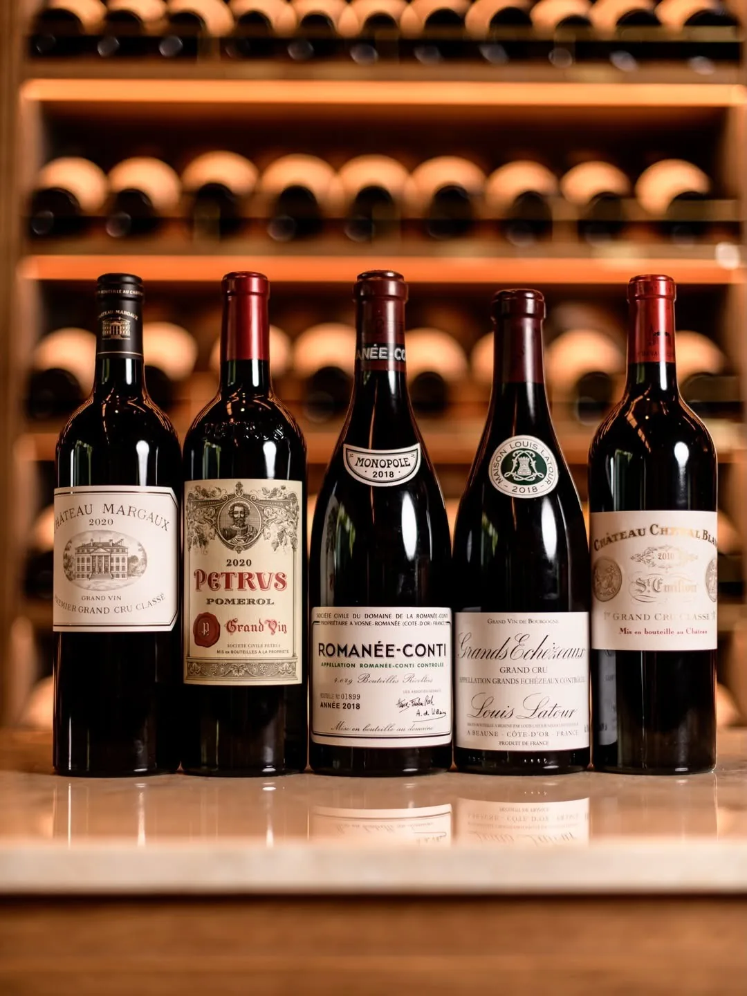 Five bottles of red wine standing in front of a wall of wine racks