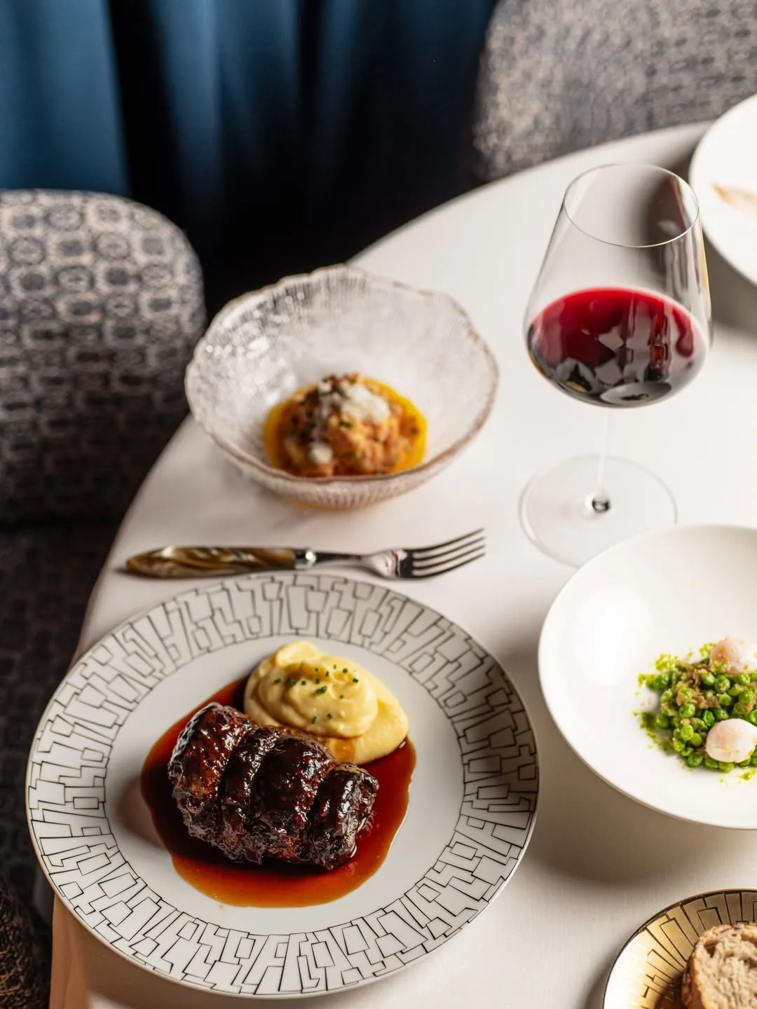 A plated meat dish with a glass of red wine on a round table
