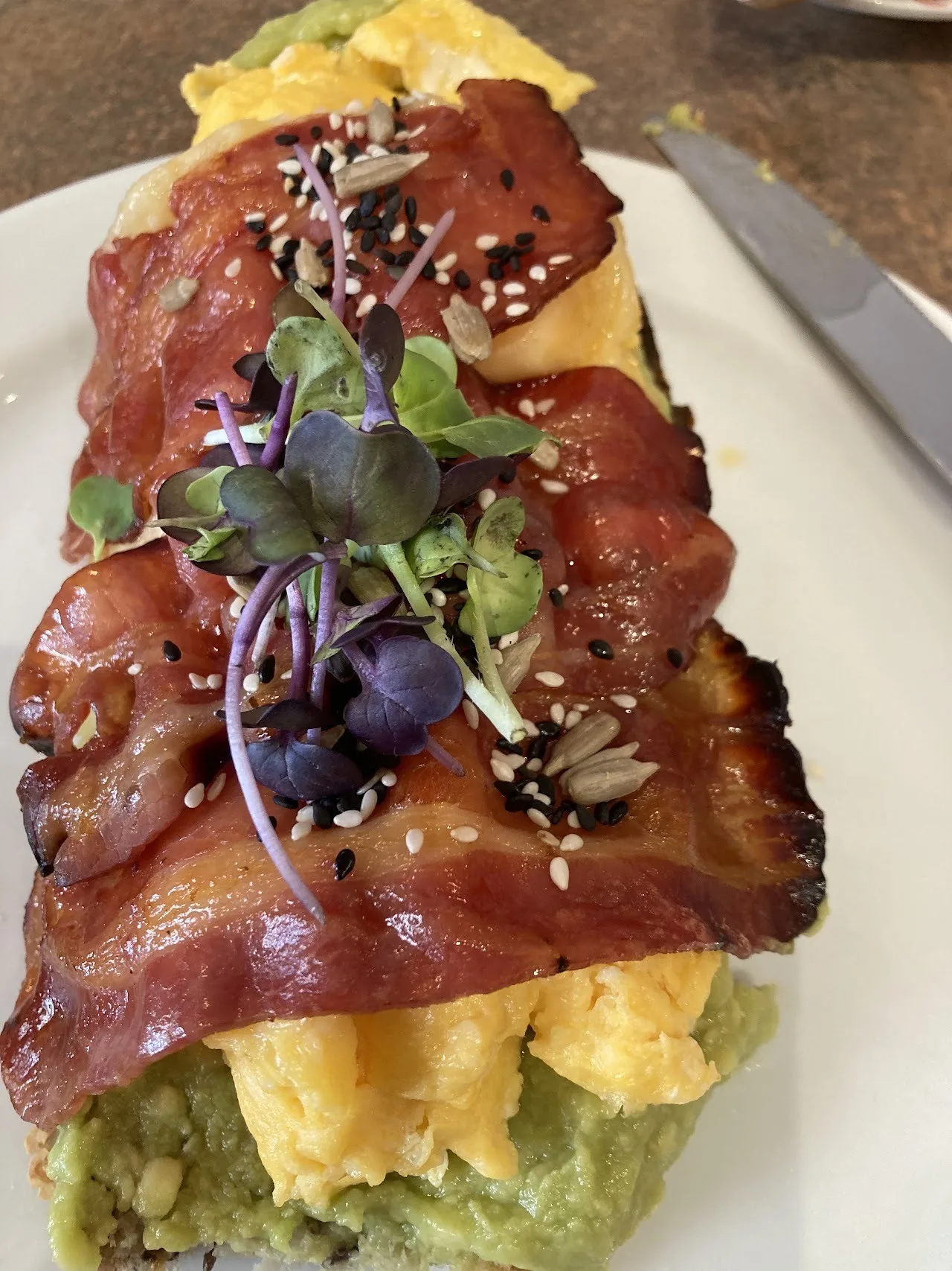 A slice of toast topped with scrambled egg, avocado, bacon and micro herbs