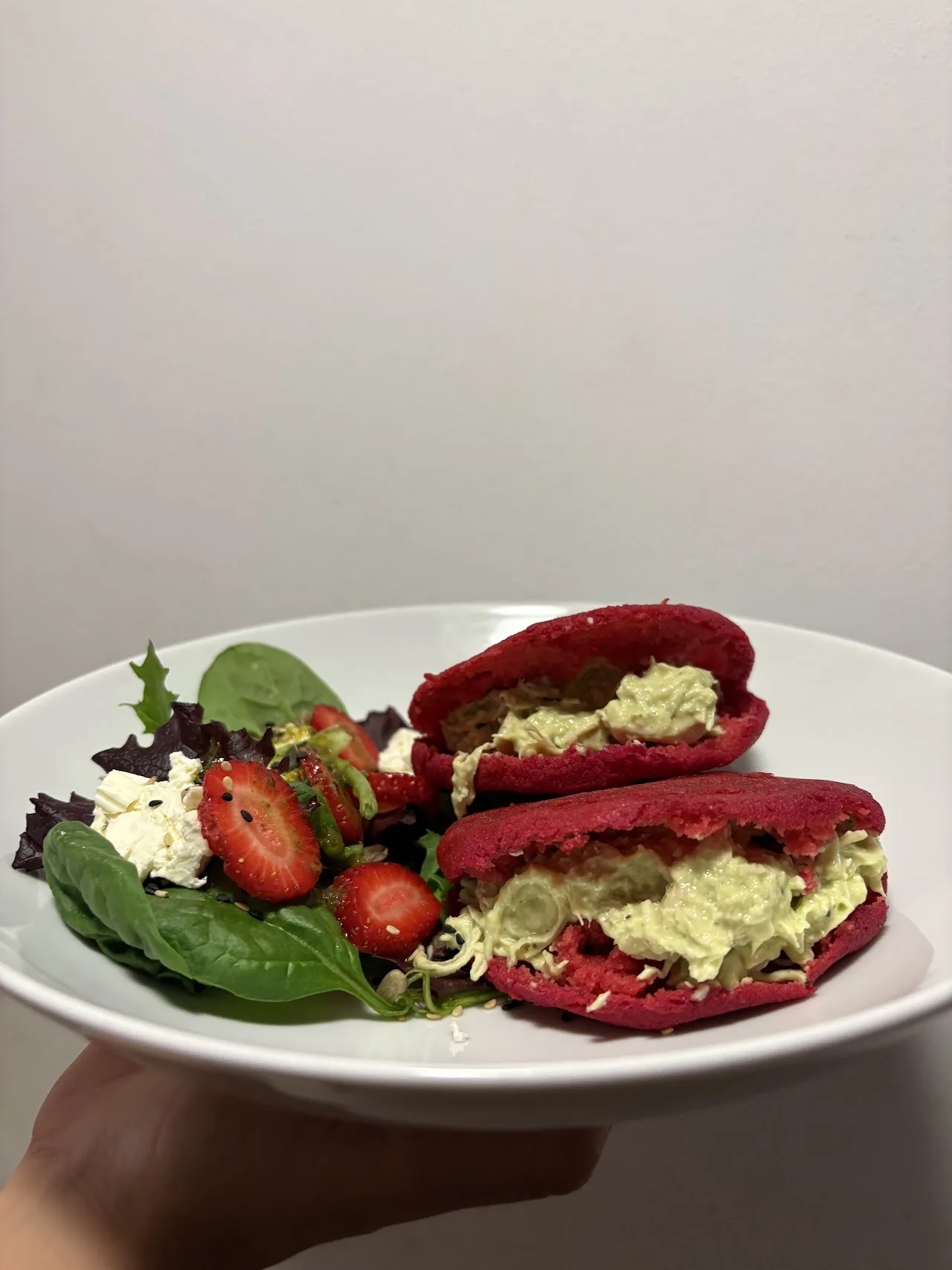 A plate of two red rounds filled with avocado, with strawberries and salad leaves