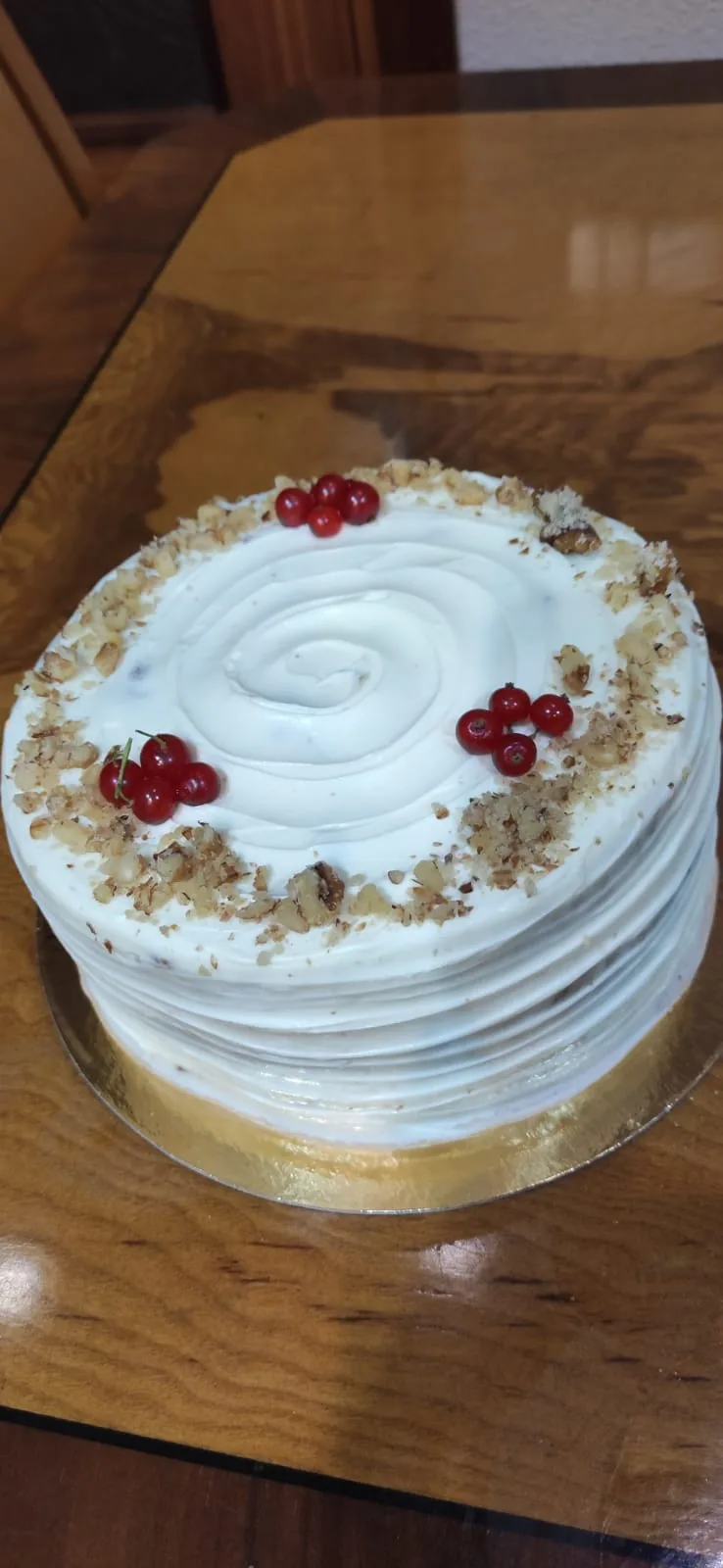 A white frosted cake topped with fresh raspberries and gold leaf