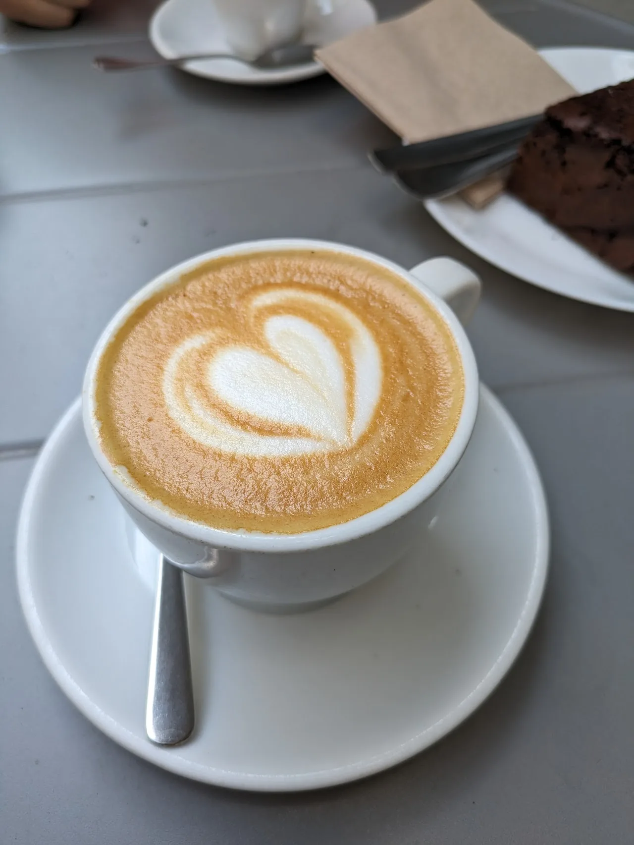 A latte with heart-shaped foam art next to a pastry