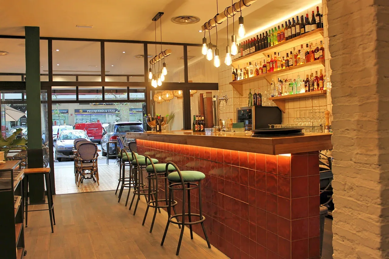 A bar counter with a lit front and green stools in a warm restaurant interior