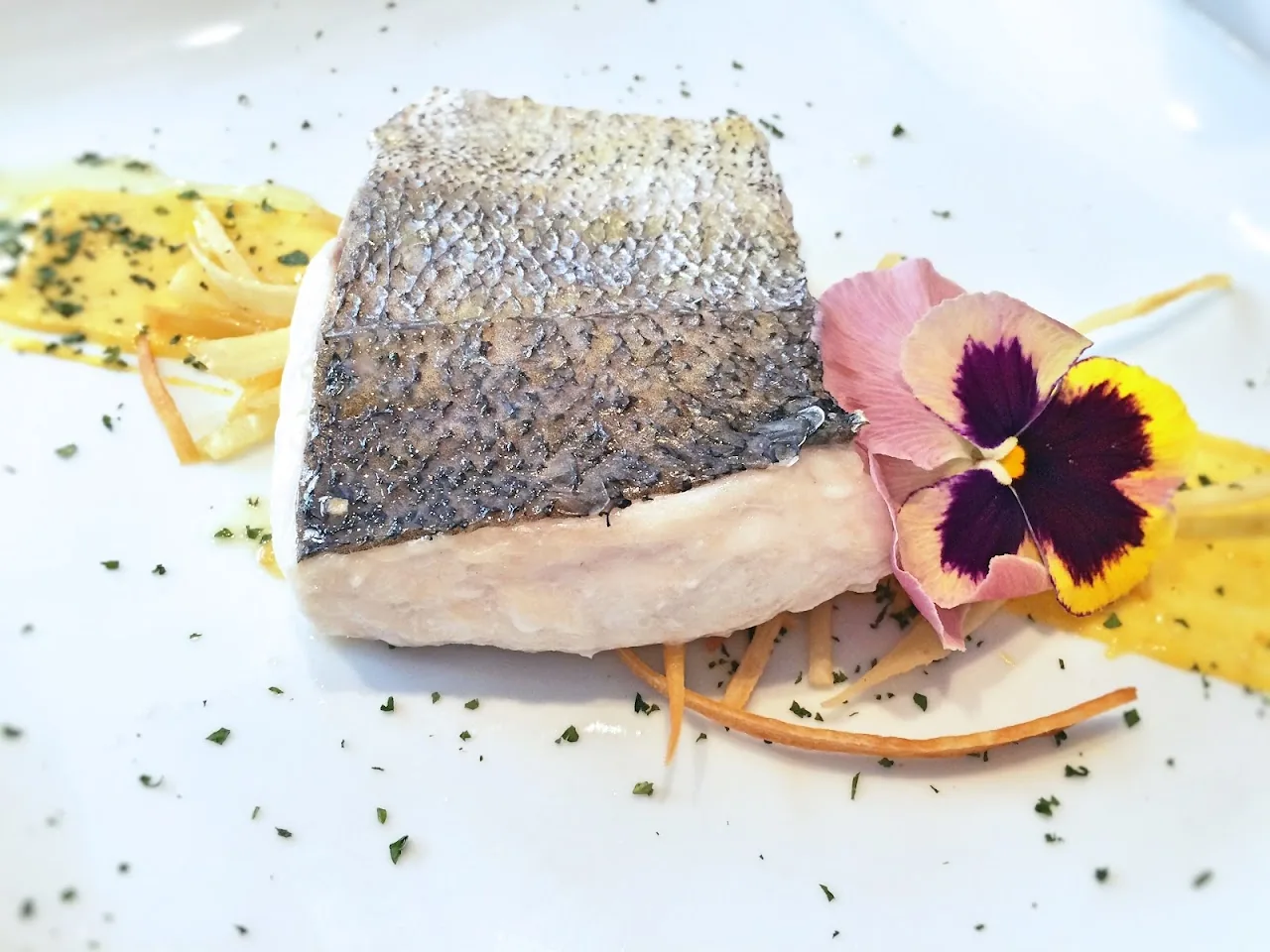A seared fish fillet with crispy skin garnished with an edible flower and citrus