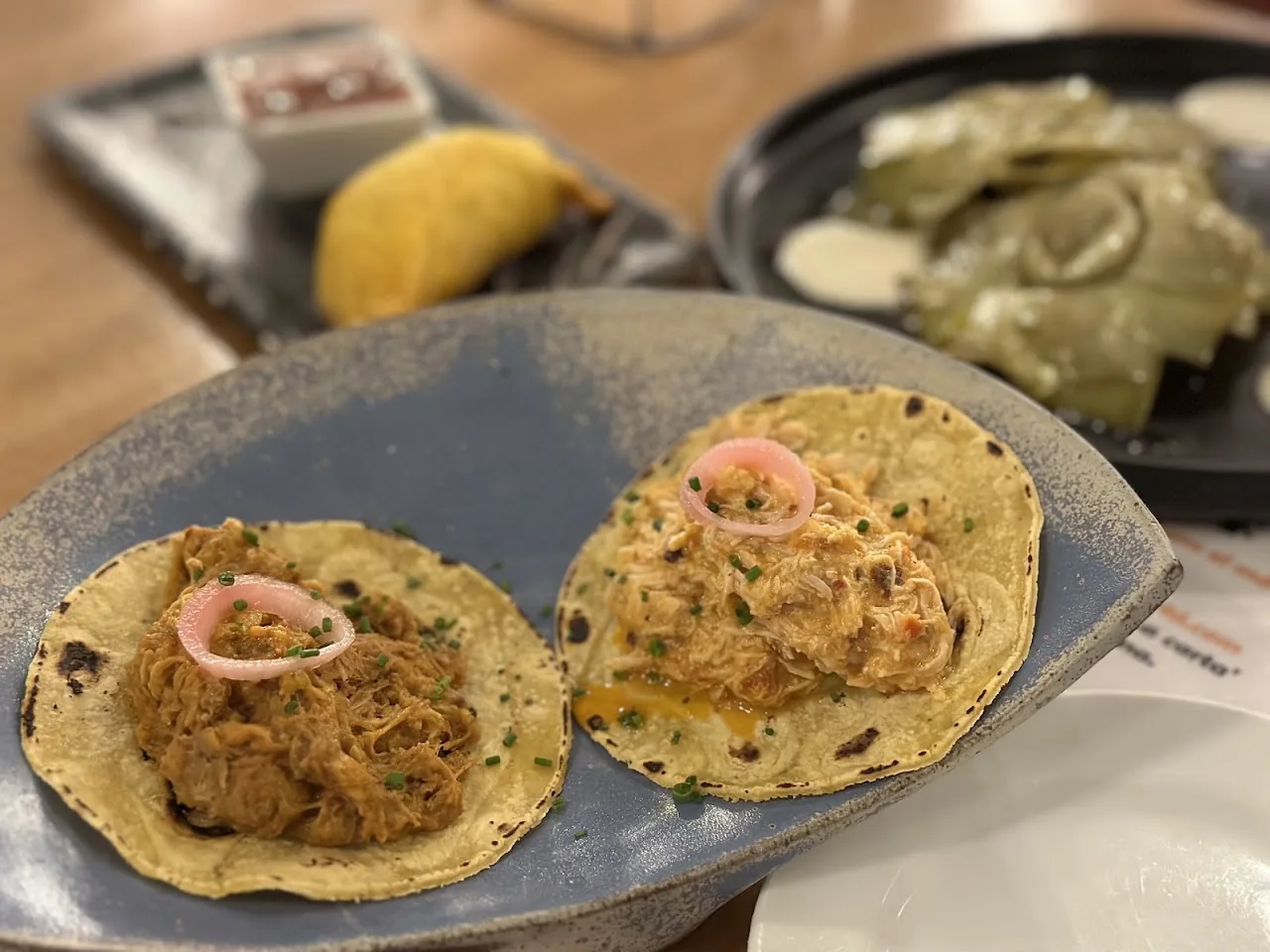 Two soft tacos topped with shredded meat and pickled red onion, served with side sauces