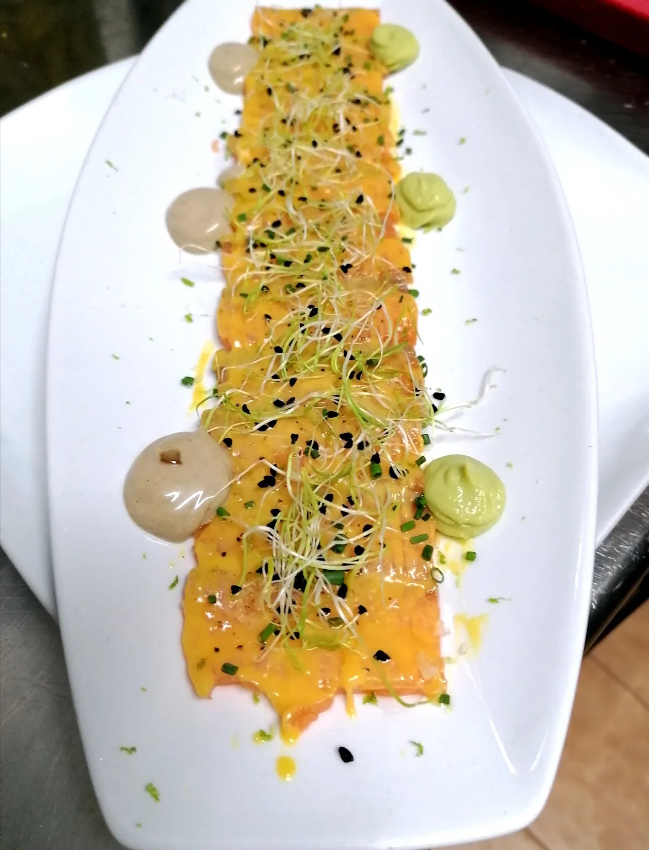 A citrus carpaccio-style dish drizzled with orange sauce and herbs