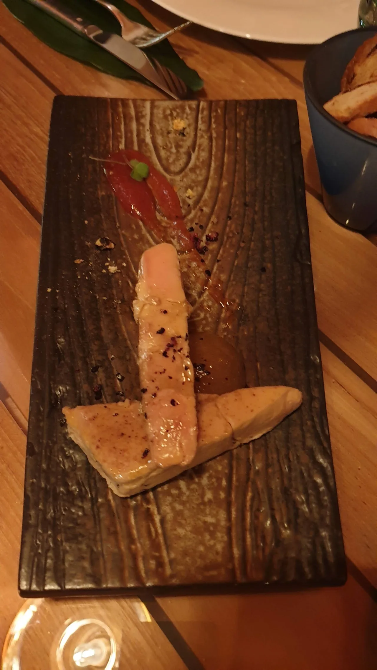 A piece of seared fish or scallop on a dark wooden board with seasoning