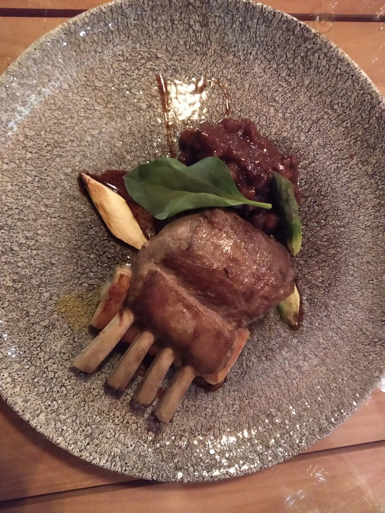 A rack of lamb chops with a dark sauce and greens