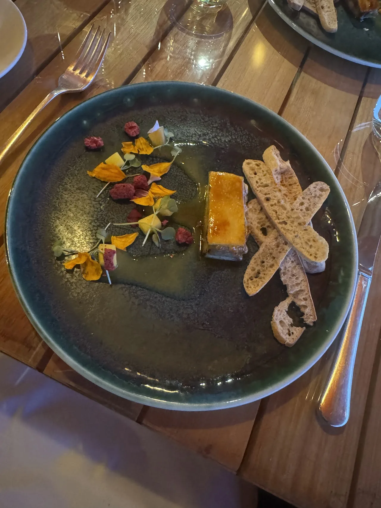 A plated dessert with a thin wafer and colorful fruit garnish