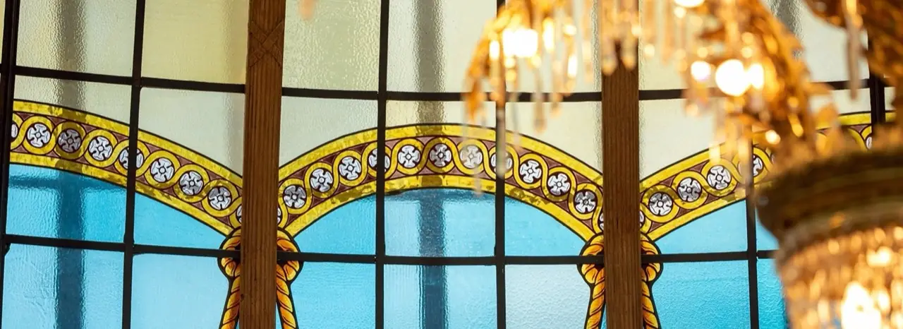 Detail of the ornate stained-glass cupola with yellow and blue leaded glass and a gilded crystal chandelier