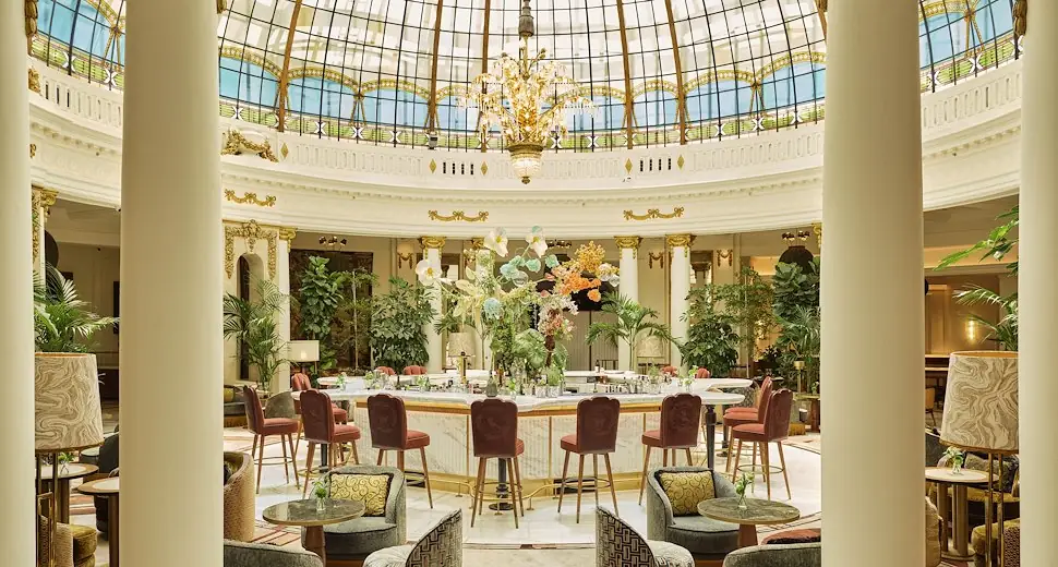 The circular Rotunda bar and lounge beneath the grand stained-glass dome, with velvet bar stools, armchairs and a floral centerpiece