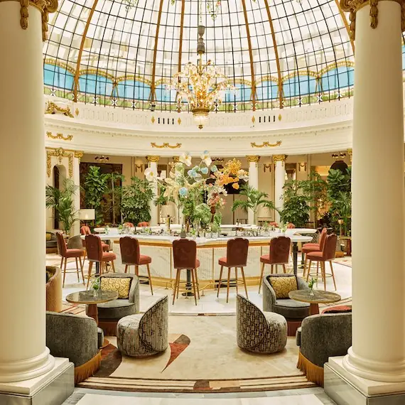 Rotunda lounge and bar under the stained-glass cupola, framed by columns with patterned armchairs and floral arrangement