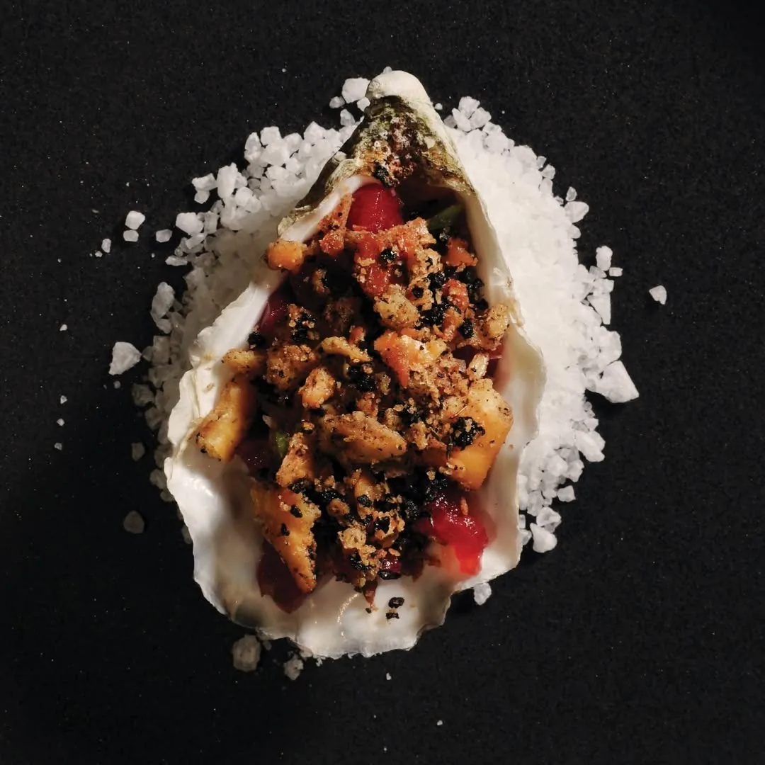 A single oyster shell topped with a crumbly garnish on a bed of coarse salt