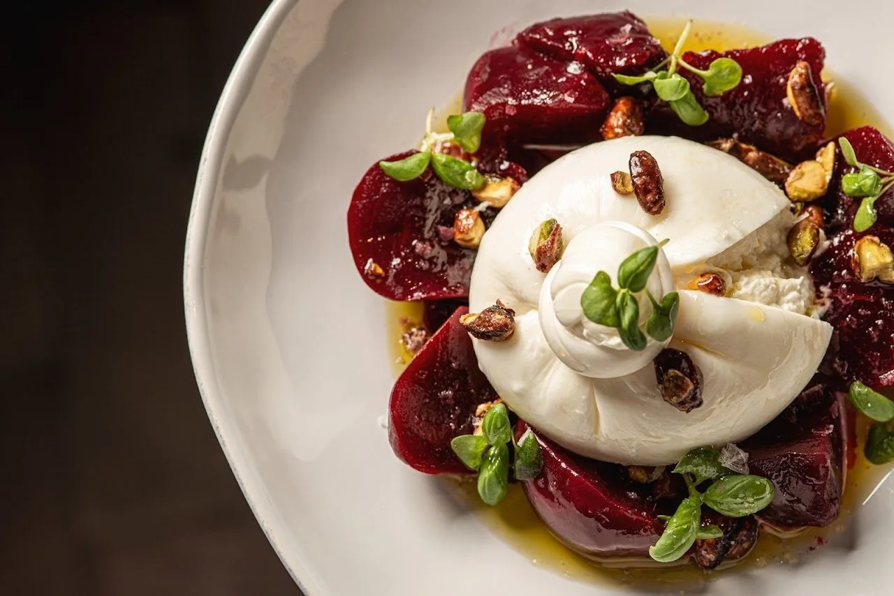 Burrata on red beetroot with nuts on a white plate