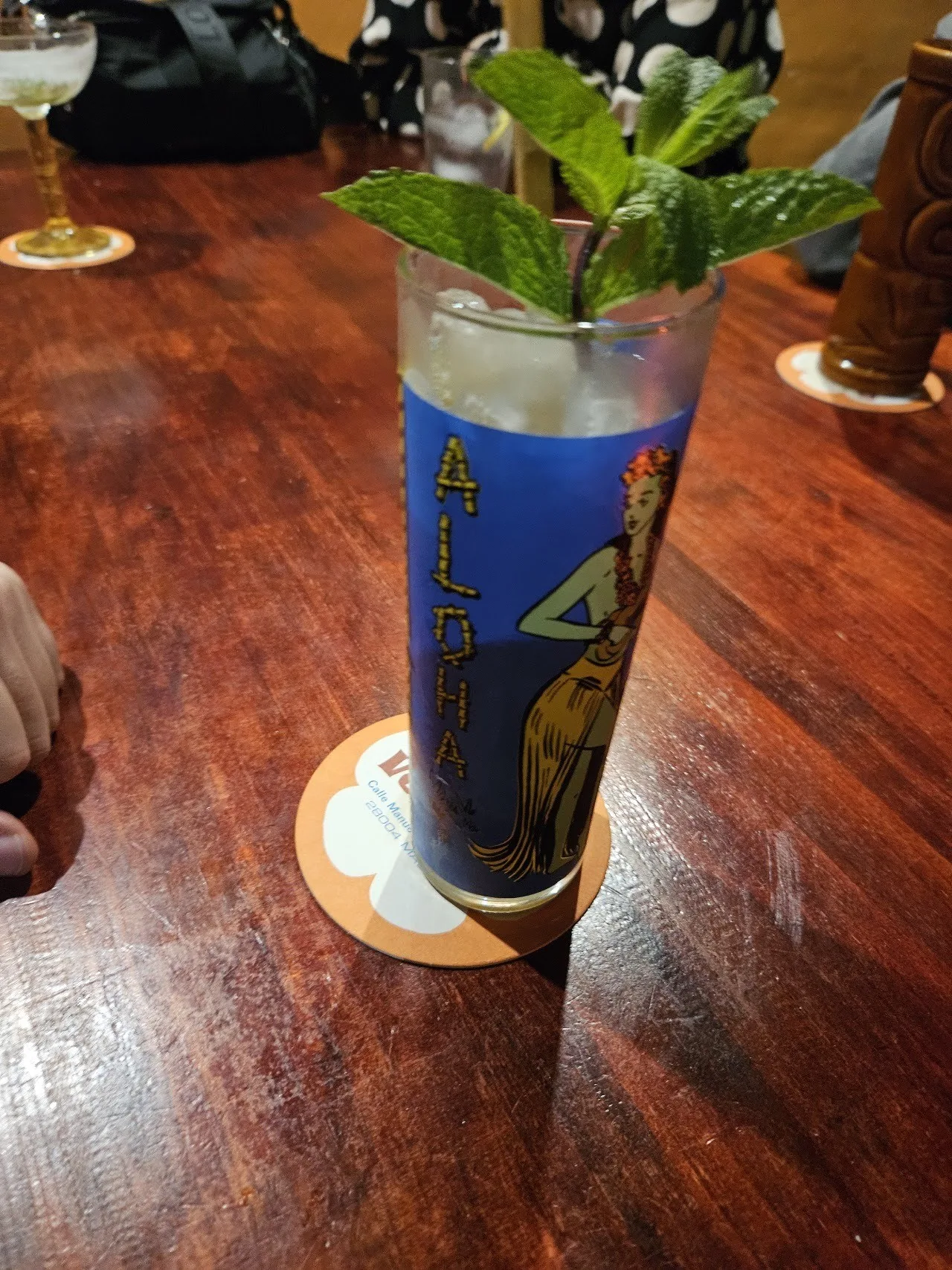 A tall blue glass cocktail with mint on a wooden bar
