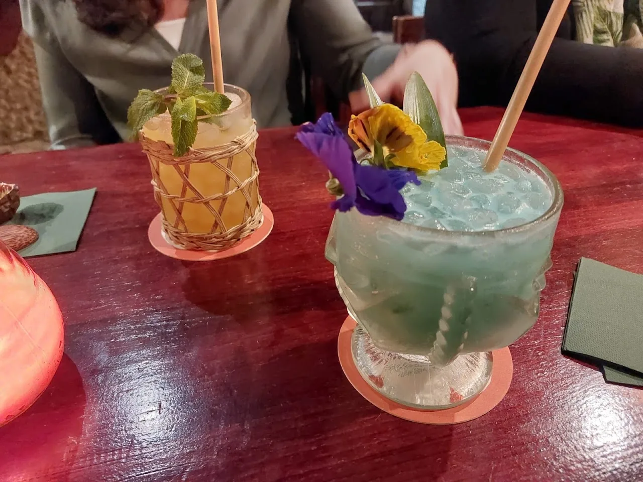Two cocktails with straws, one garnished with an edible flower