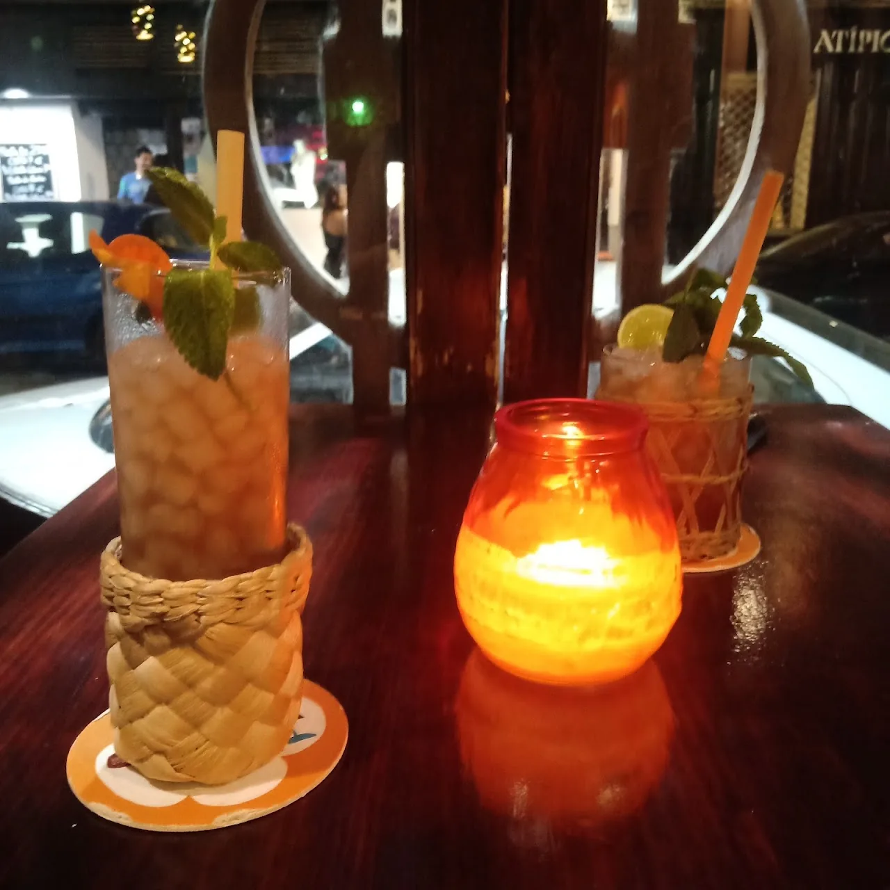 Two tiki cocktails in carved wooden-style mugs beside a candle