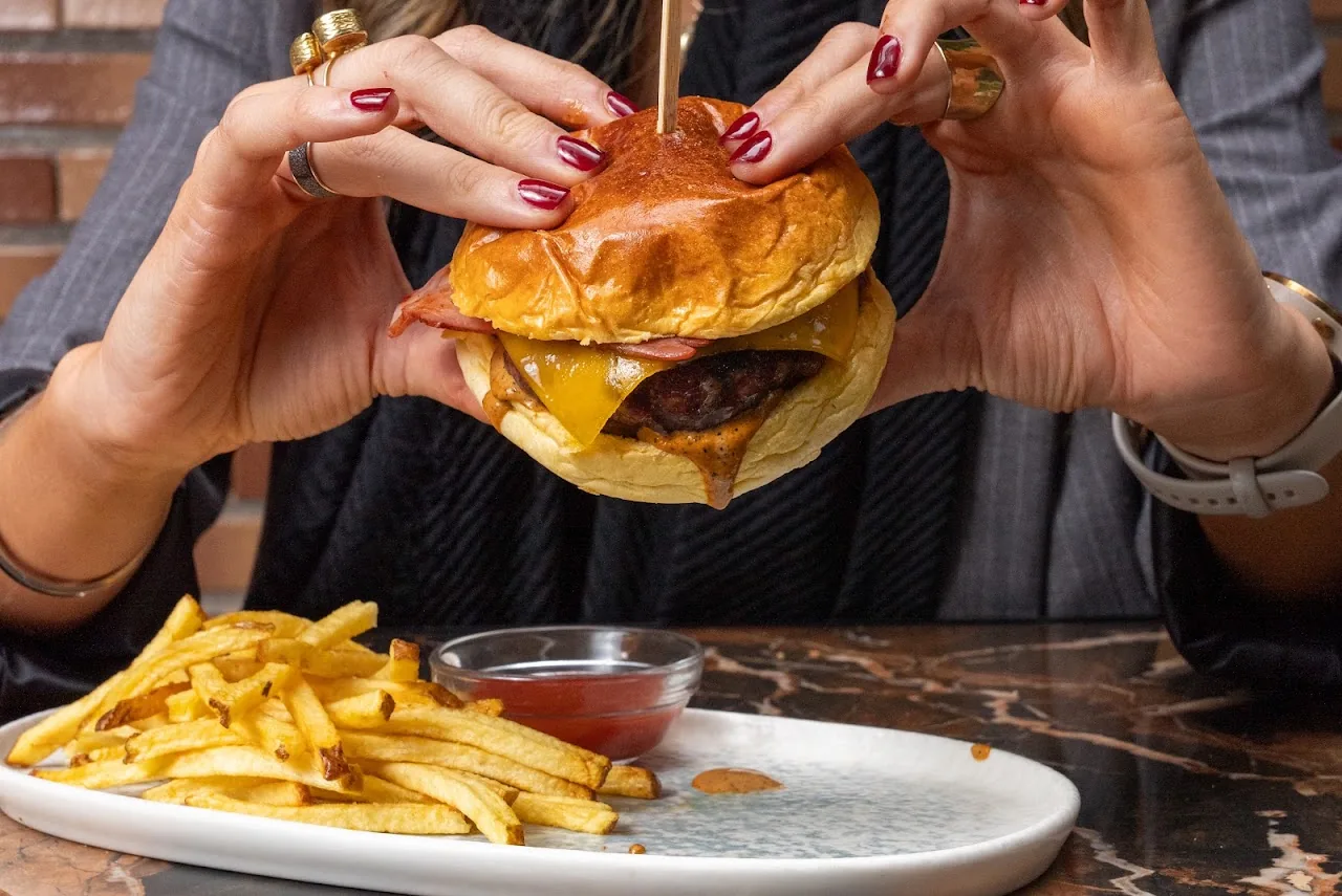 A burger held in two hands with a side of fries