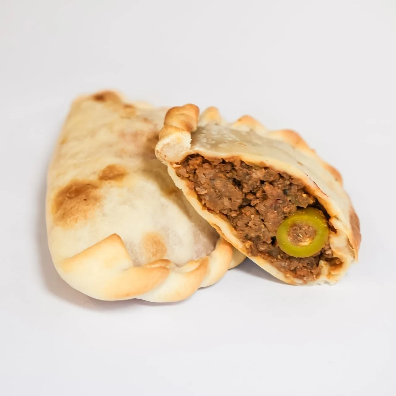 A baked empanada cut open to show a meat filling with an olive, on a white background