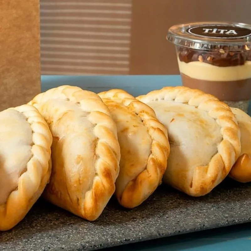A row of baked empanadas with braided edges on a grey tray