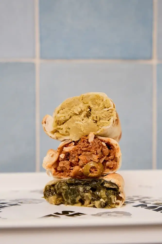 Three empanadas cut open and stacked, revealing chicken, spiced beef with green olive, and creamed spinach fillings