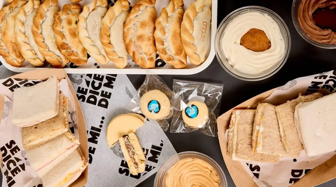 Overhead spread of Argentine food: tray of empanadas, crustless sandwiches, alfajores and cups of dulce de leche
