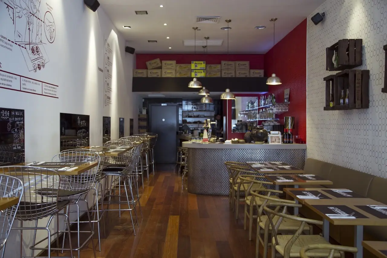 Dining room at Tlaxcal with a long bar, wooden tables and a red back wall