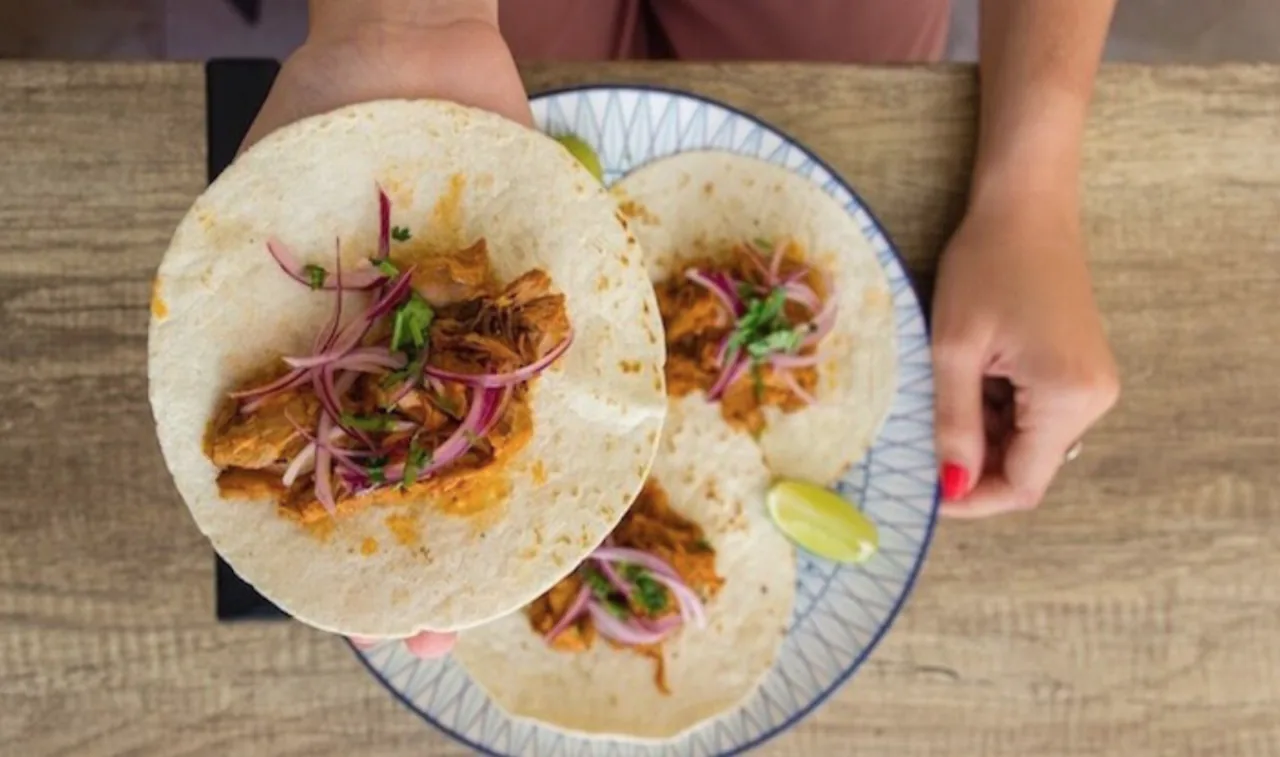 Tacos with shredded meat and pickled onion held in hand, top-down view