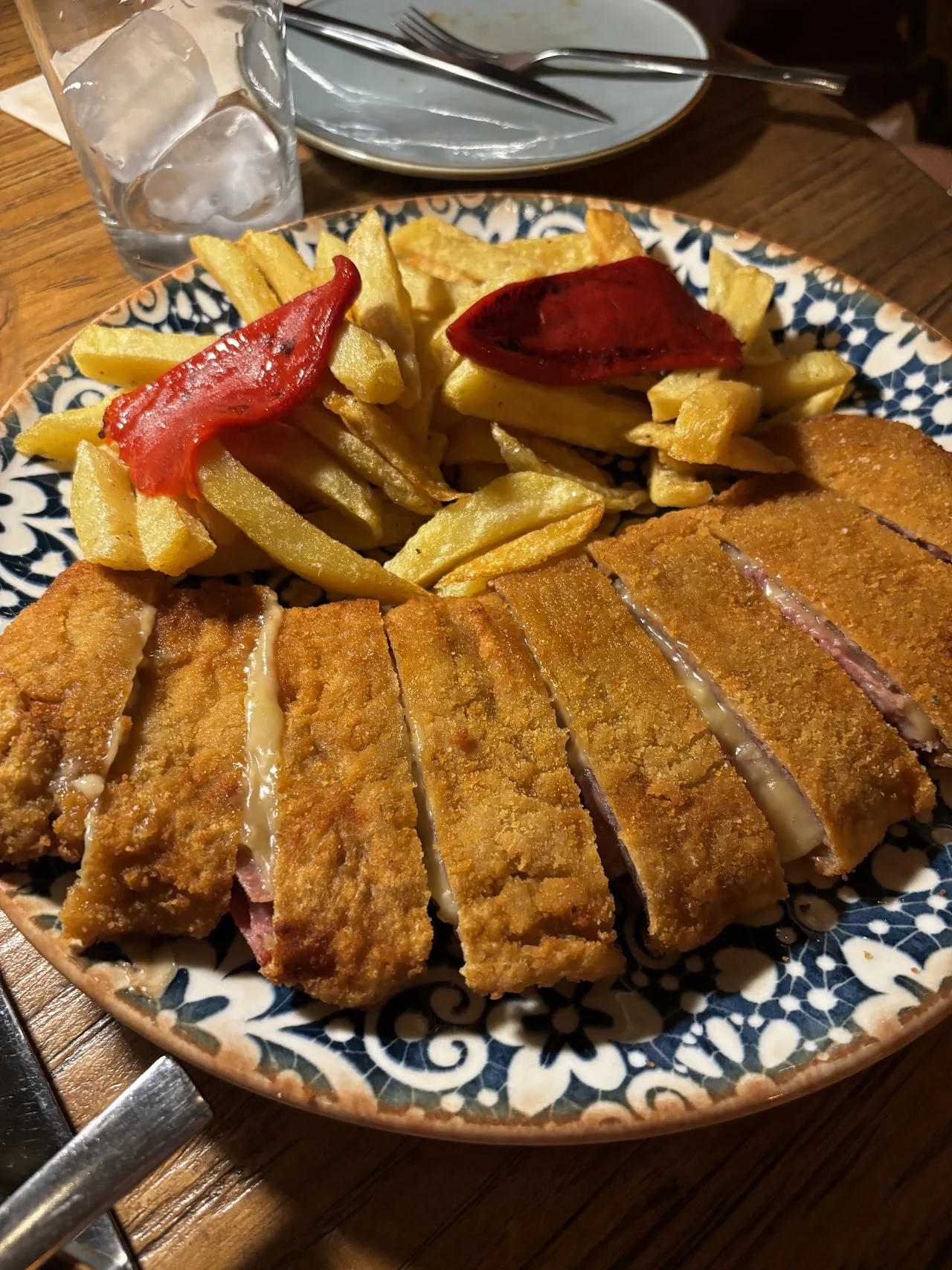 A breaded veal cutlet (cachopo) sliced open, served with fries and roasted red peppers