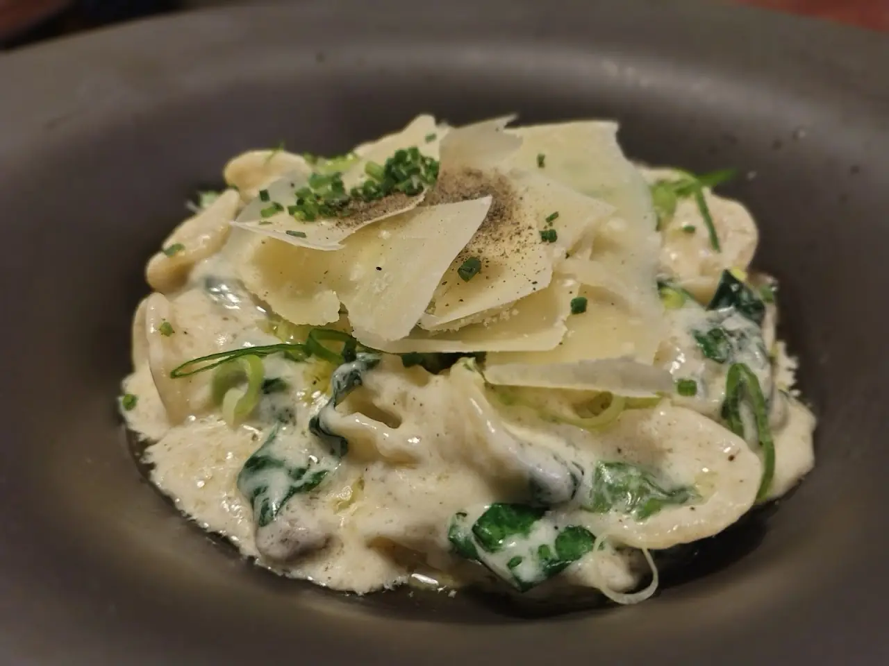 Creamy pasta with shaved cheese and greens in a dark bowl
