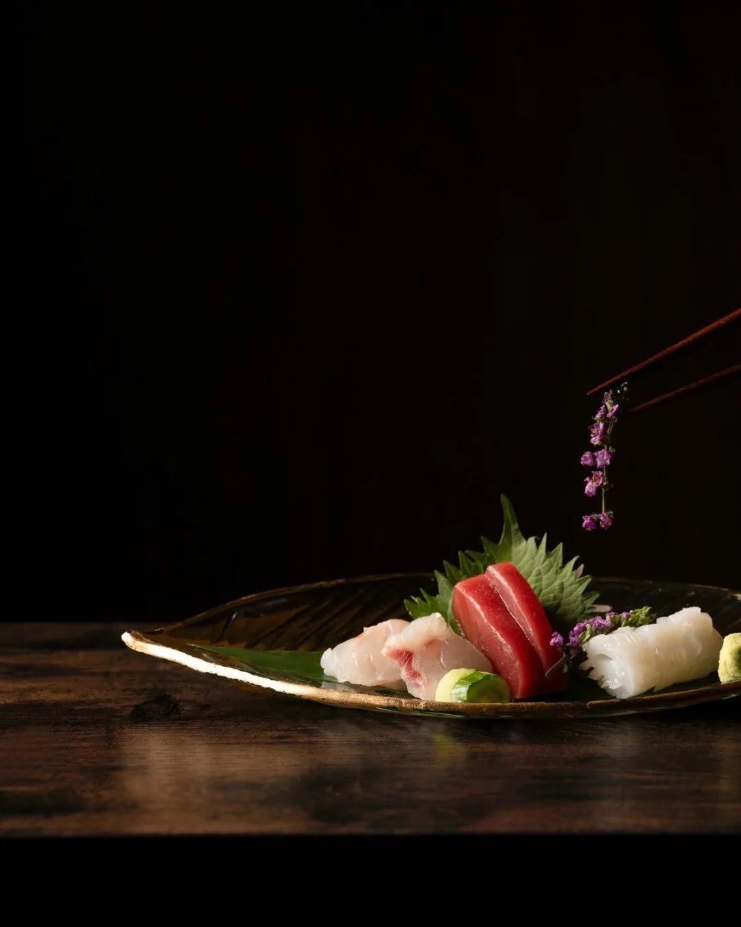 A dark plate of assorted sashimi slices with green garnish