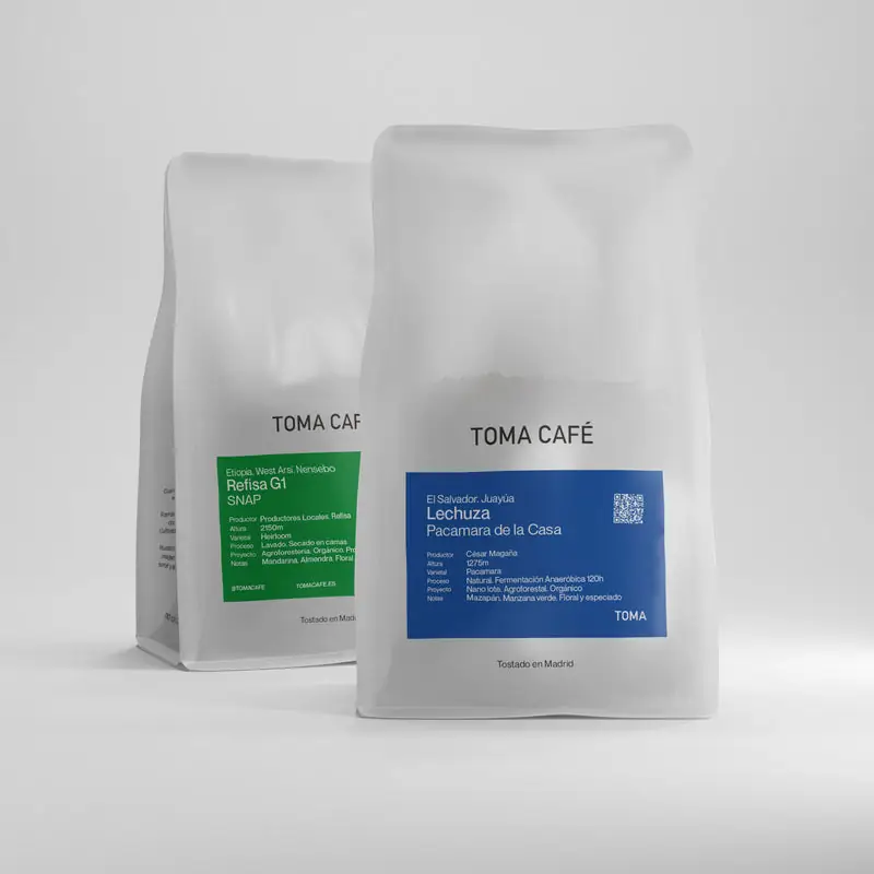 Two Toma Café coffee bags (Refisa G1 and Lechuza) on a light studio background, retail product shot