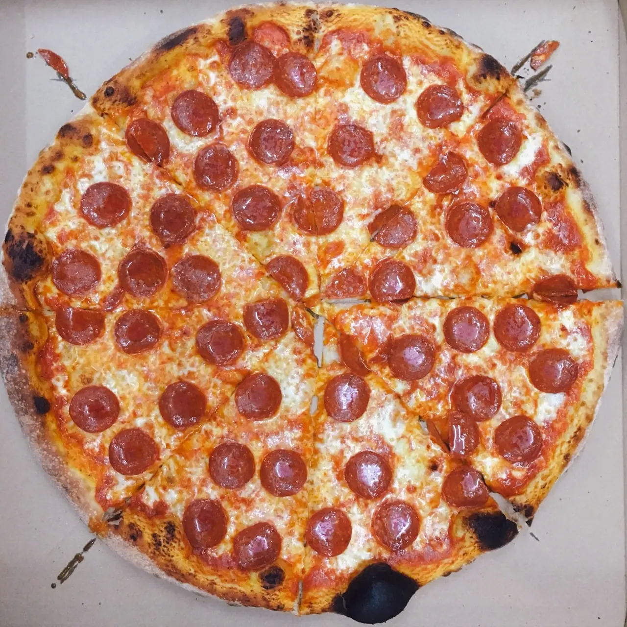 Whole New York-style pepperoni pizza with charred crust, melted mozzarella, and glossy pepperoni cups, cut into eight slices in an open box, at Tomasso - New York Pizza.