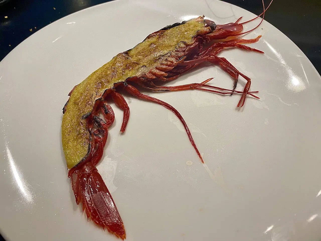 A whole grilled red prawn served on a white plate.