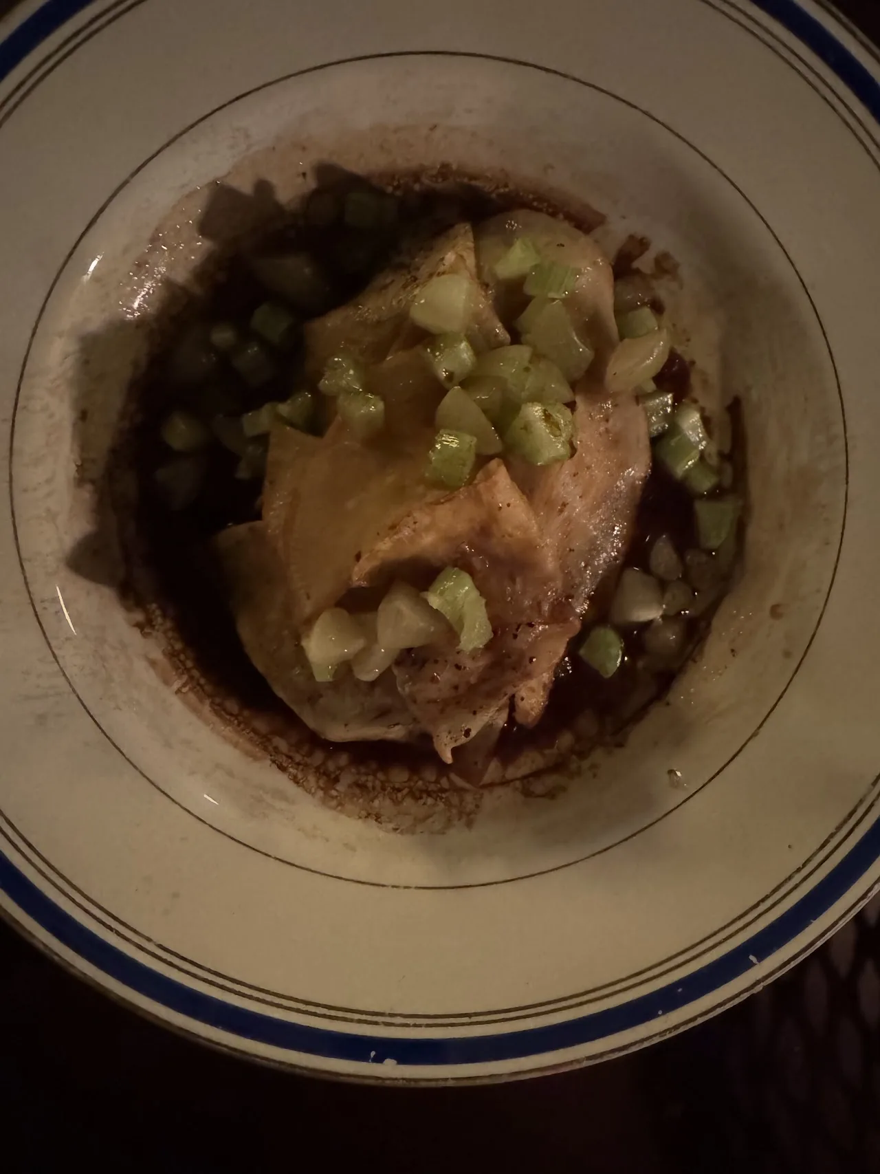 A dish of meat in broth topped with chopped green herbs