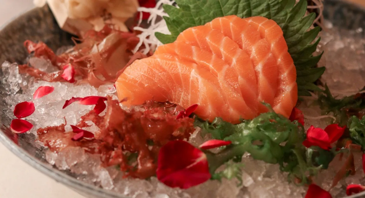 A plate of salmon sashimi on crushed ice with garnishes