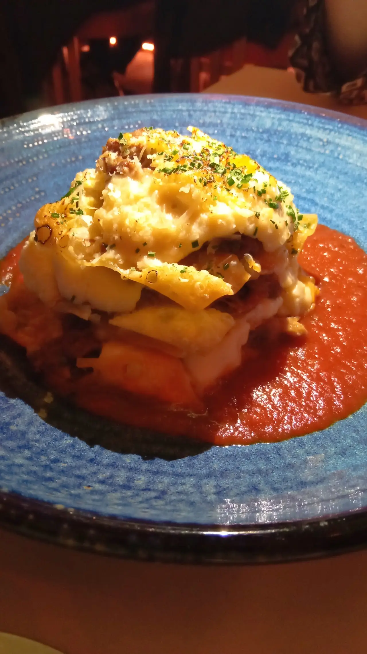 A layered baked dish with melted cheese on top, served over tomato sauce on a blue plate.