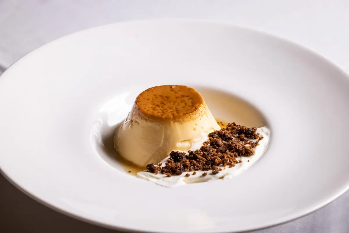 A caramel flan dessert on a white plate with a crumble garnish.