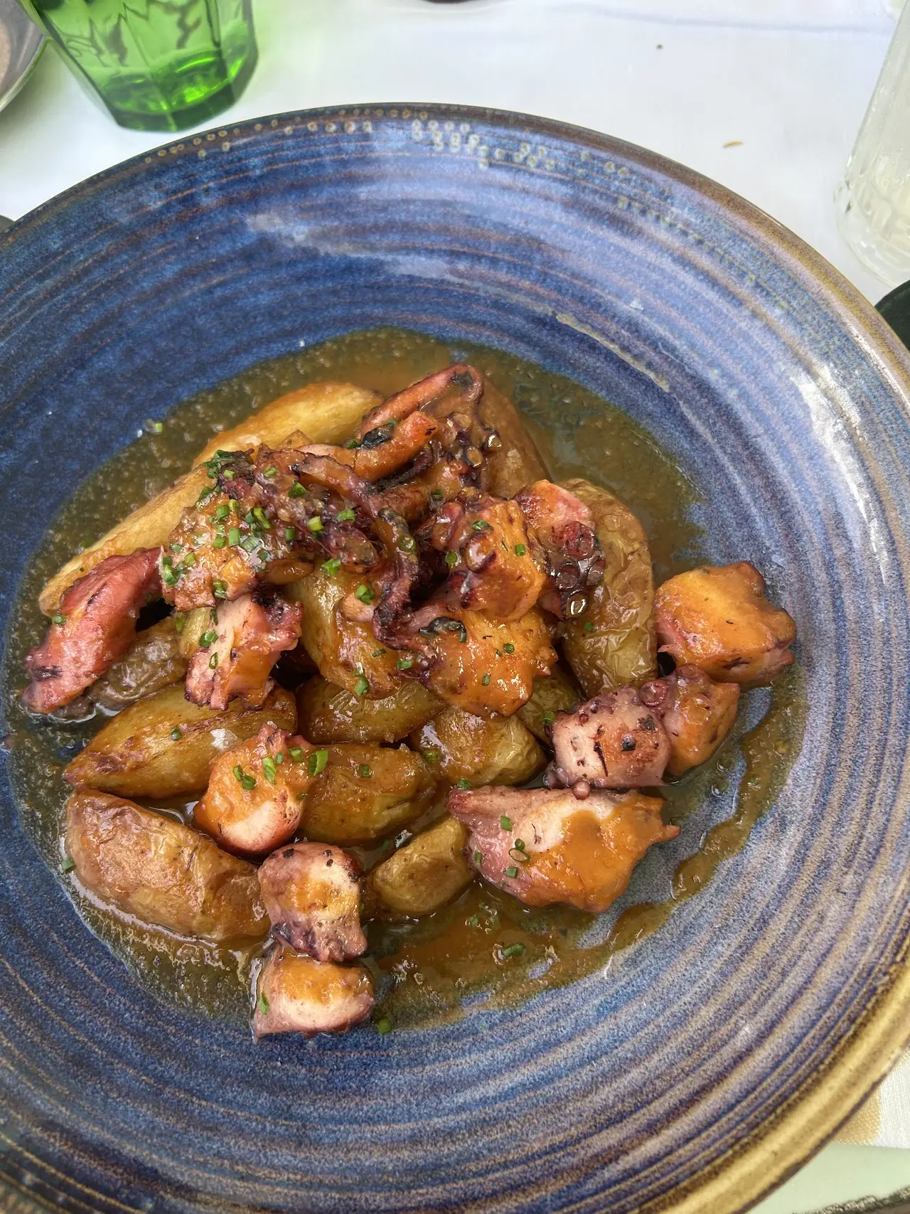 Grilled octopus and potatoes in a light sauce on a blue ceramic plate.